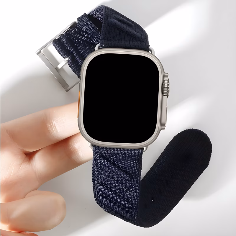 Bracelet Apple Watch EzStrap en nylon tissé de style sport avec boucle métallique en titane et motif ondulé, tenu entre les doigts sur fond blanc lumineux.
