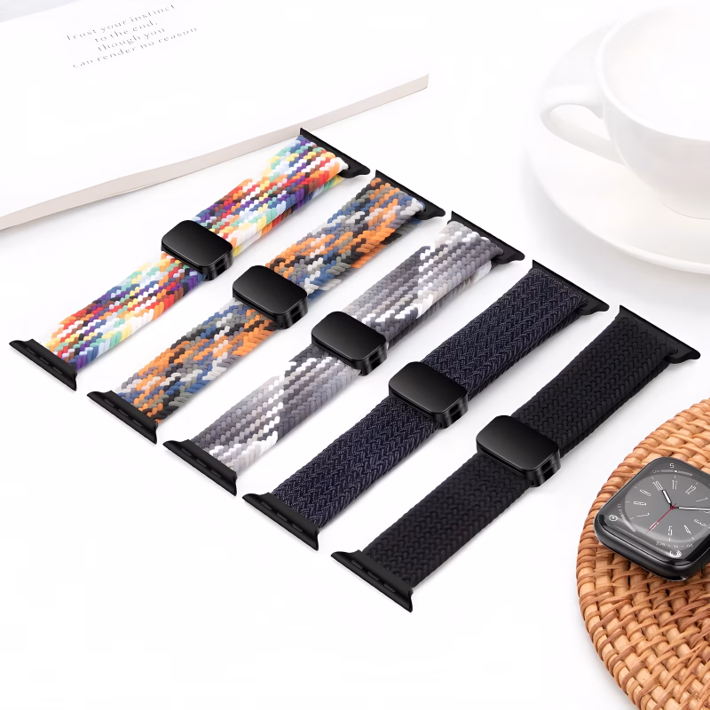 Bracelet Apple Watch EzStrap en nylon texturé, style sport, décliné en plusieurs motifs tressés colorés, présenté aligné sur une table blanche à côté d'une tasse et d'une montre.