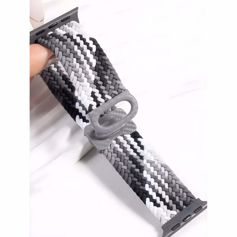 Bracelet Apple Watch EzStrap en plastique tressé, style sport avec motif texturé noir, gris et blanc, tenu en gros plan devant une surface blanche.