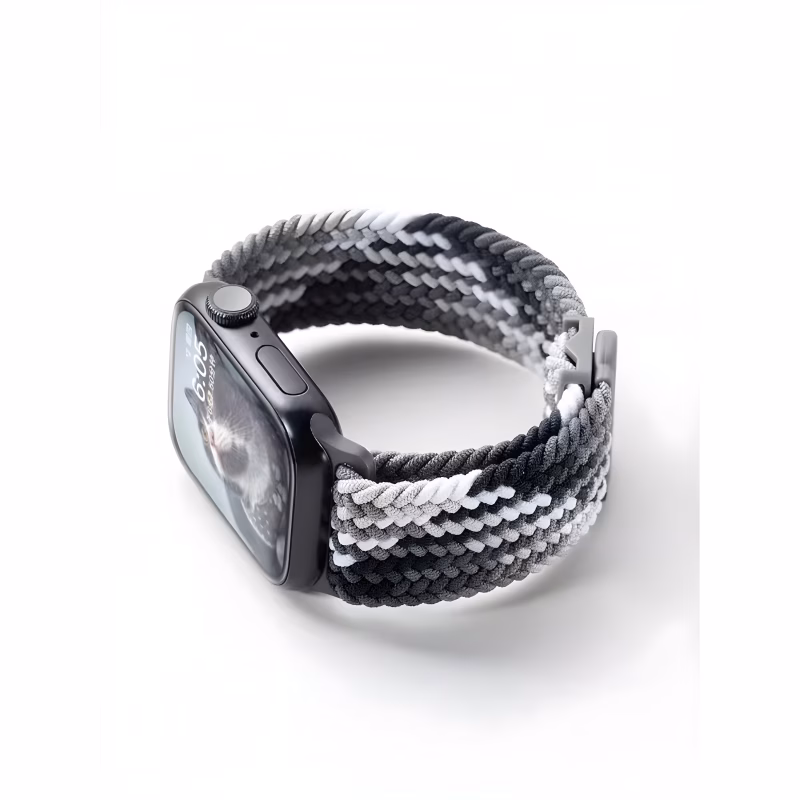 Bracelet Apple Watch EzStrap en nylon tressé à dominante noire, grise et blanche, de style sport texturé, présenté en gros plan posé sur une surface blanche.