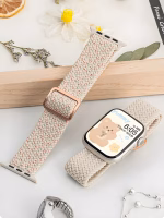 Bracelet Apple Watch EzStrap en nylon tressé de style sport, avec texture texturée et boucle réglable rose doré, posé sur une surface claire à côté d’éléments décoratifs fleuris.
