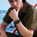 Bracelet Apple Watch EzStrap en silicone noir au design sport ondulé, porté au poignet d’un homme assis en extérieur près de la mer.