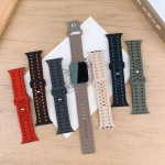 Bracelets Apple Watch EzStrap en silicone perforé au design sportif, déclinés en plusieurs coloris, présentés à plat sur une table en bois autour d'une montre connectée.