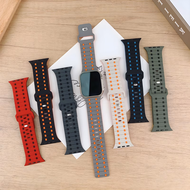 Bracelets Apple Watch EzStrap en silicone perforé au design sportif, déclinés en plusieurs coloris, présentés à plat sur une table en bois autour d'une montre connectée.