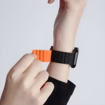 Bracelet Apple Watch EzStrap en silicone ondulé bicolore noir et orange, style sport, porté au poignet d’une personne ajustant la fermeture magnétique.