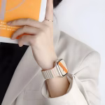 Bracelet Apple Watch EzStrap en silicone blanc au design ondulé, style sport, porté au poignet d’une femme vêtue d’un blazer clair tenant un magazine.