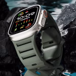 Bracelet Apple Watch EzStrap en silicone mat perforé de style sport, présenté en gros plan sur fond de roches sombres au bord de l’eau.