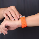 Bracelet Apple Watch EzStrap en silicone mat orange au design perforé, style sport, porté au poignet d’un homme en t-shirt noir.
