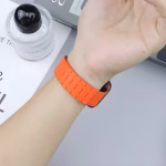 Bracelet Apple Watch EzStrap en silicone orange, au style sport avec design texturé segmenté, porté au poignet d’une personne dans un environnement lumineux et minimaliste.