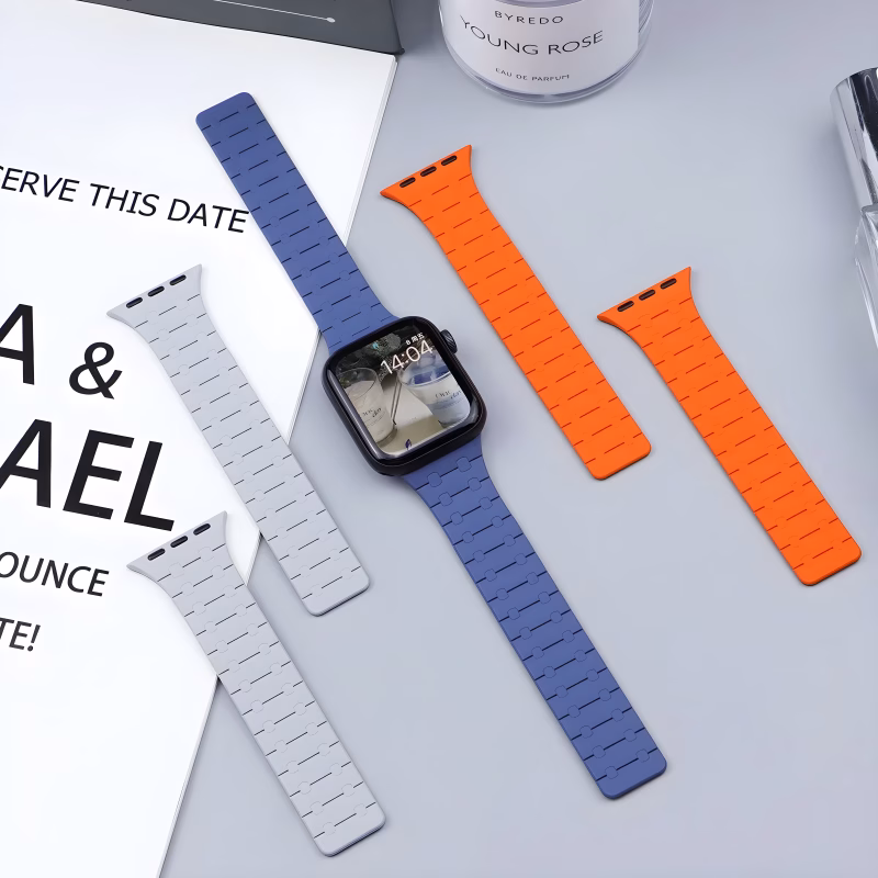 Bracelet Apple Watch EzStrap en silicone texturé de style sport, décliné en plusieurs couleurs, posé à plat sur une table grise avec une montre connectée et des accessoires autour.