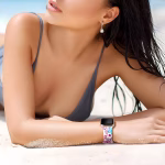 Bracelet Apple Watch EzStrap en silicone souple à design fantaisie perforé, style sport avec motifs imprimés colorés, porté au poignet d’une femme allongée sur le sable à la plage.