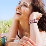 Bracelet Apple Watch EzStrap en silicone souple à design fantaisie perforé, style sport avec motif imprimé floral, porté par une femme allongée en extérieur sous le soleil.