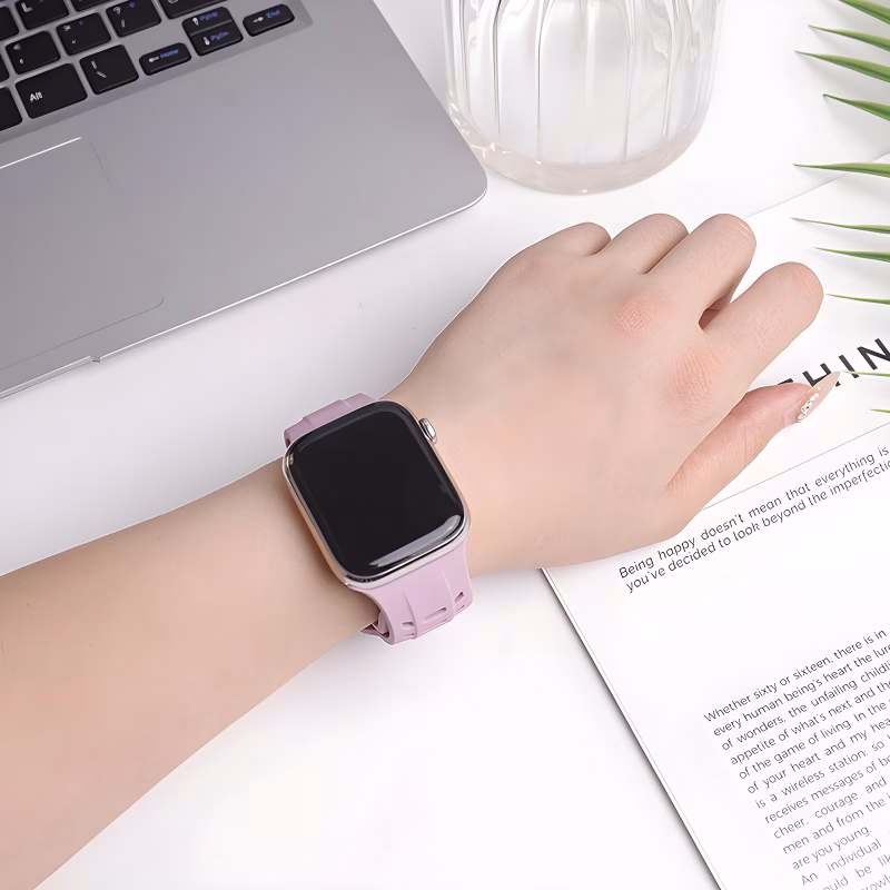 Bracelet Apple Watch EzStrap en silicone rose souple de style sport, avec ouvertures ventilées, porté au poignet d’une femme travaillant sur un bureau blanc.