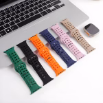 Bracelets Apple Watch EzStrap en silicone perforé de style sport, déclinés en plusieurs couleurs et posés sur un bureau près d’un ordinateur portable et d’une montre.