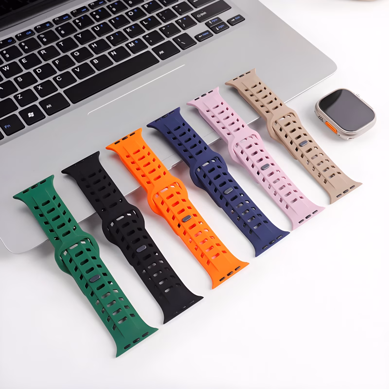 Bracelets Apple Watch EzStrap en silicone perforé de style sport, déclinés en plusieurs couleurs et posés sur un bureau près d’un ordinateur portable et d’une montre.