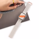 Bracelet Apple Watch EzStrap en silicone souple blanc à structure ondulée, de style sport, posé sur une surface blanche à côté d'une main féminine tenant un magazine.