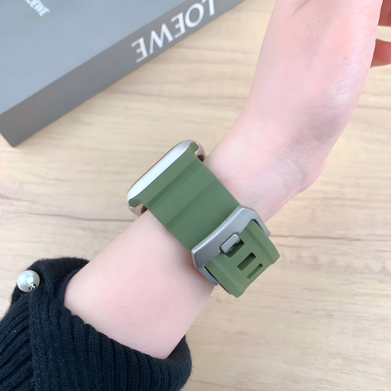 Bracelet Apple Watch EzStrap en silicone vert, au style sport avec fentes horizontales, porté au poignet d’une personne sur fond de table en bois clair.
