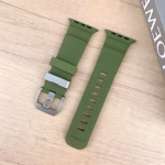 Bracelet Apple Watch EzStrap en silicone lisse vert olive, style sport avec fentes horizontales, posé sur une table en bois clair à côté d’un livre.