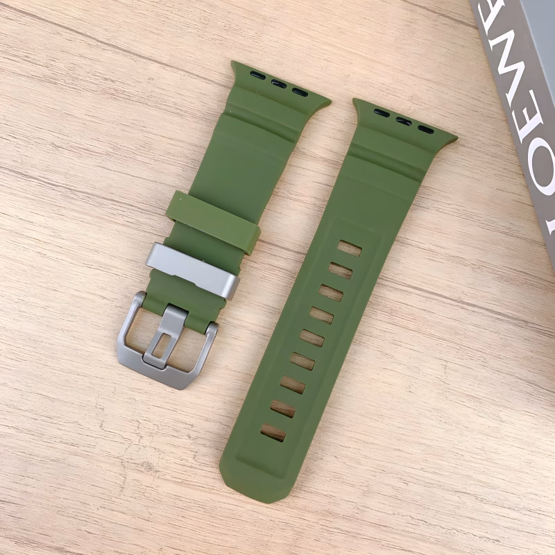 Bracelet Apple Watch EzStrap en silicone lisse vert olive, style sport avec fentes horizontales, posé sur une table en bois clair à côté d’un livre.