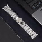 Bracelet Apple Watch EzStrap en titane brossé, style luxe à maillons articulés, posé à plat sur un bureau en cuir près d’un ordinateur portable.