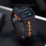Bracelet Apple Watch EzStrap en métal noir au style sportif, avec une bande orange centrale, présenté en gros plan sur une surface texturée noire.